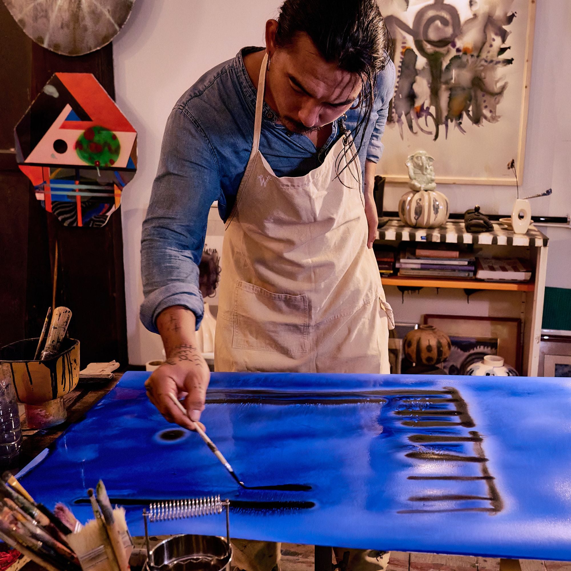 Eakarin in his art studio, he is wearing the Wiseguy Original Apron in the color Beige and is painting.