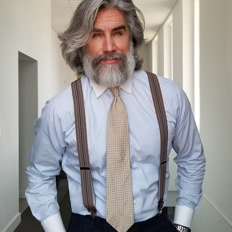 Man wearing Brown Striped Wiseguy Suspenders over a blue striped shirt styled with a tie in a white room