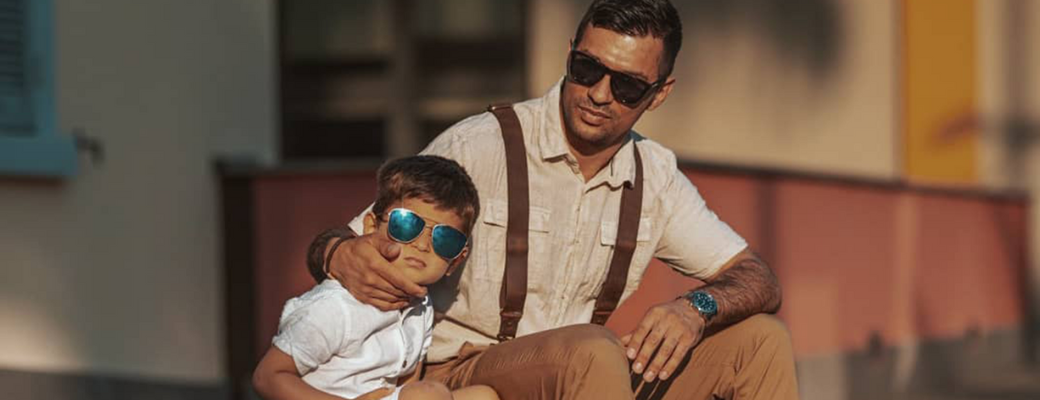 Man and his son both standing in front of brick wall, both wearing suspenders