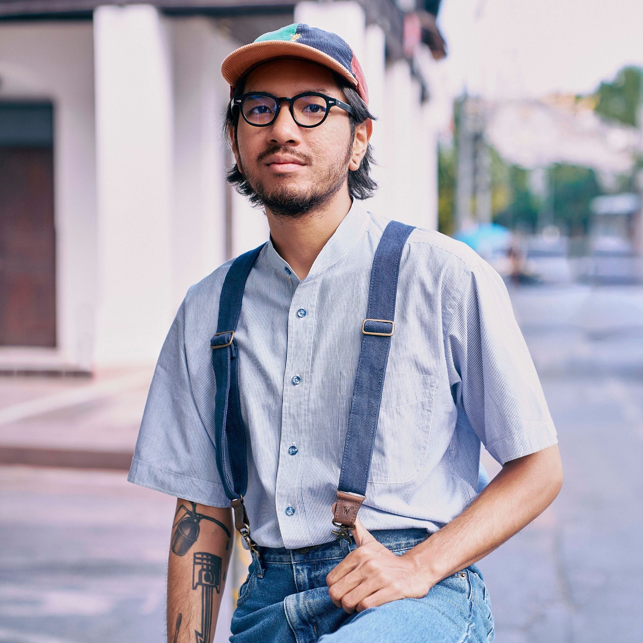 Man wearing blue striped shirt, navy blue suspenders and jeans, looking in the camera